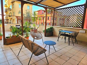 An outdoor patio with a table and chairs, surrounded by potted plants.