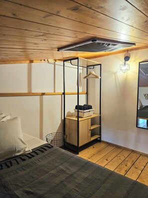 Une pièce comprenant un lit, une armoire en bois, un portant à vêtements et un luminaire fixé au mur.