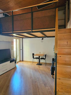 Une pièce avec un plafond en bois, une table à manger avec des chaises, un canapé et un escalier.