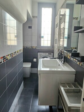 A bathroom with a white sink, a mirror, a window, and a washing machine.