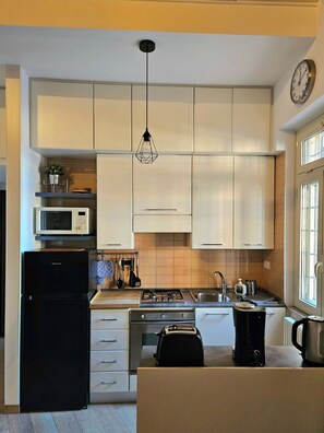 Une cuisine moderne avec des meubles blancs, un réfrigérateur noir, un four à micro-ondes, une cuisinière et un évier.