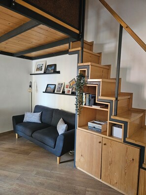 Un salon moderne avec un canapé bleu foncé, un escalier en bois et des étagères intégrées où sont disposés des livres et des photos encadrées.