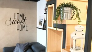 A modern living room with a grey sofa, a wooden bookshelf with decorative items, and a wall with the text "HOME Sweet HOME". - DELICIOUS LOFT TO SAN PIETRO (Roma)