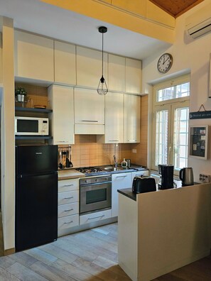 Une cuisine moderne avec des armoires blanches, un réfrigérateur noir, un four à micro-ondes, une cuisinière et un évier. Il y a une horloge au mur et une fenêtre donnant sur l’extérieur.