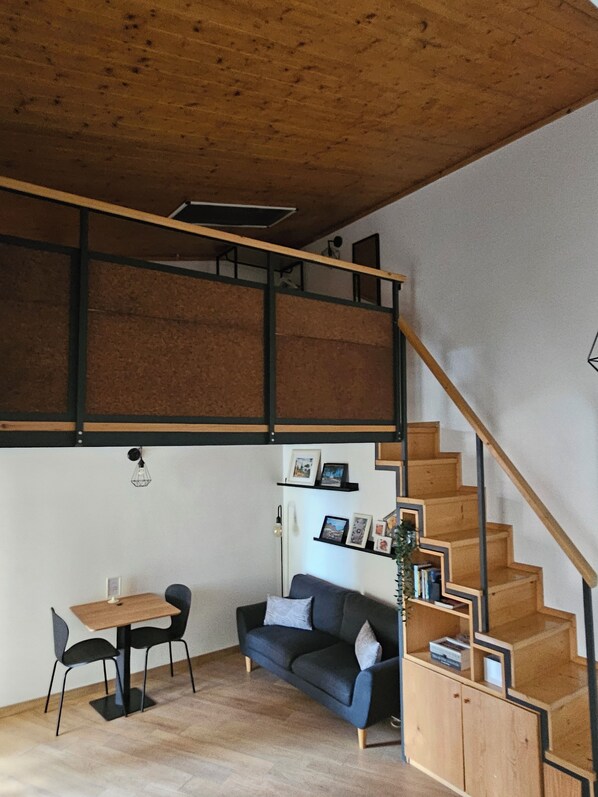 A loft-style room with a wooden staircase, a sofa, a dining table, and a bookshelf. - DELICIOUS LOFT TO SAN PIETRO (Roma)