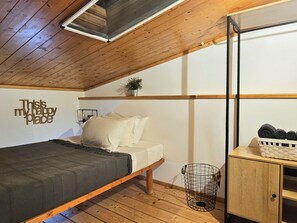 A bedroom with a bed, a bedside table with a basket, a wall-mounted shelf with a plant, and a ceiling fan.