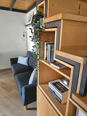 Un salon moderne avec un canapé bleu foncé, une bibliothèque en bois et une plante suspendue.