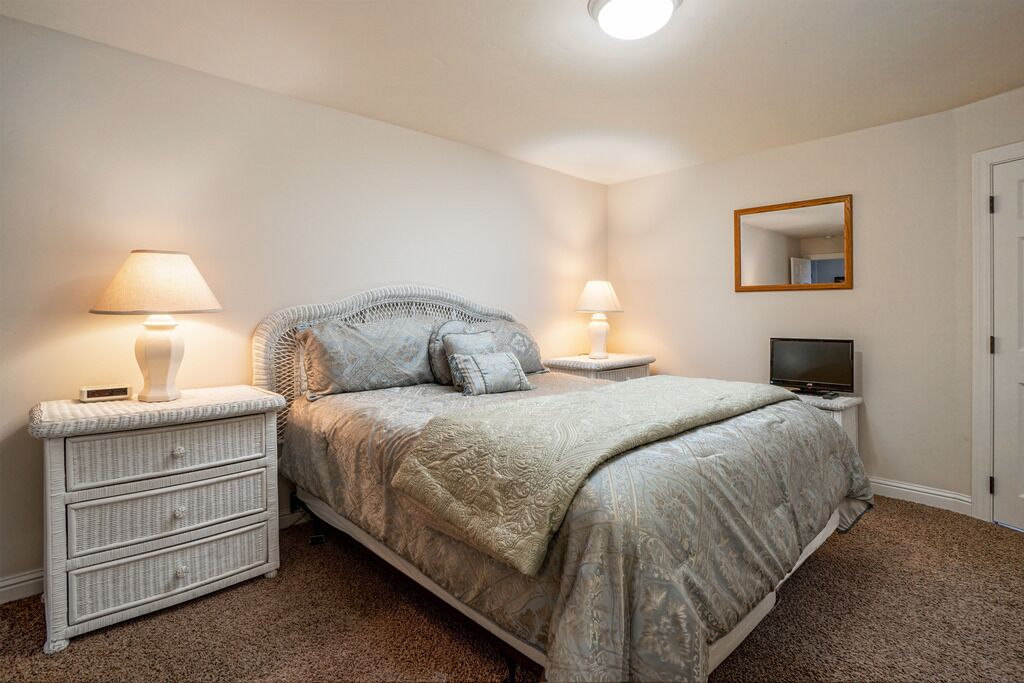 A bedroom with a bed, two bedside tables with lamps, a TV, and a mirror on the wall.