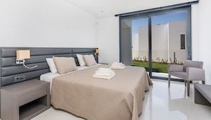 Una habitación de hotel moderna con una cama grande, mesitas de noche, un escritorio y una silla. Cuenta con una puerta corrediza de vidrio que da a un área exterior.