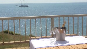 A wooden deck with a table set for a drink, overlooking a calm sea with a sailboat in the distance. - Breathtaking Ocean Views,  Luxury Beachside Apartment, Freshwater Bay -  AONB (Freshwater Bay)