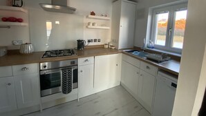 A modern kitchen with white cabinets, a stainless steel range, a built-in oven, a dishwasher, and a window providing a view of the outdoors. - Breathtaking Ocean Views,  Luxury Beachside Apartment, Freshwater Bay -  AONB (Freshwater Bay)