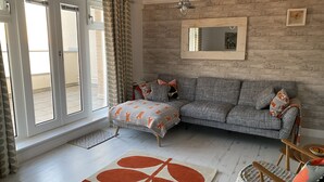 A living room with a grey sofa, a patterned rug, and a wooden floor. - Breathtaking Ocean Views,  Luxury Beachside Apartment, Freshwater Bay -  AONB (Freshwater Bay)