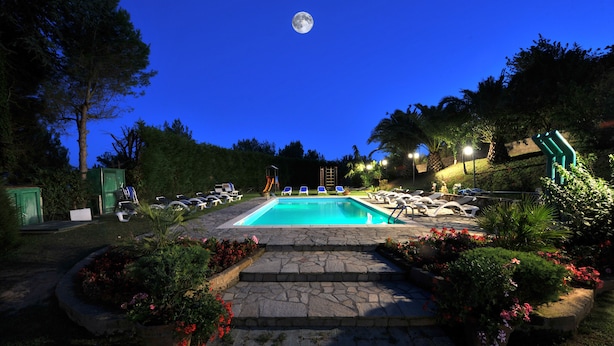 Área de piscina à noite com vista nítida da lua, cercada por espreguiçadeiras e plantas em vasos.