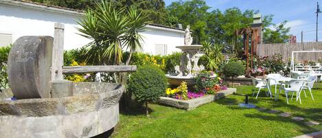 A well-maintained garden with a fountain, various plants, and outdoor seating.