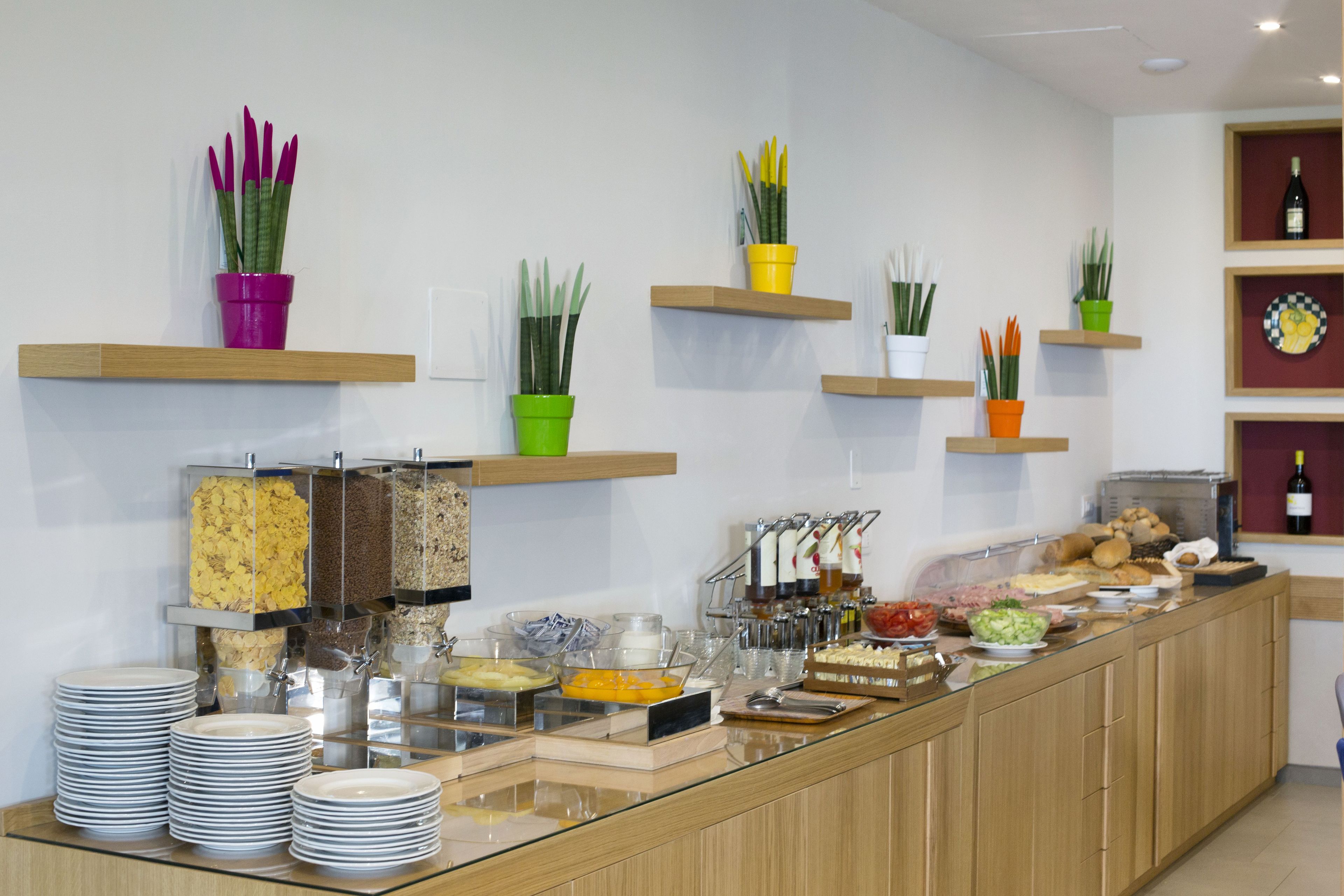 A buffet area with various food items and utensils, including bowls of cereal, fruits, and a selection of drinks.