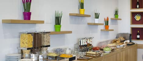Ein Buffetbereich mit verschiedenen Speisen und Geschirr, darunter Schüsseln mit Müsli, Obst und einer Auswahl an Getränken.