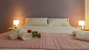 A neatly made bed with white linens and a pink bedspread, two bedside lamps, and a wall sign that reads "Mr. & Mrs."