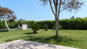 A landscaped garden with a paved area, a variety of trees, and a stone structure.
