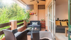 Un balcon doté de meubles en osier, d’un ventilateur de plafond et offrant une vue sur la verdure.