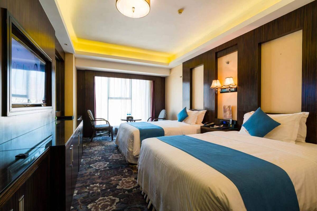 A hotel room with two beds, a desk, a chair, and a TV.