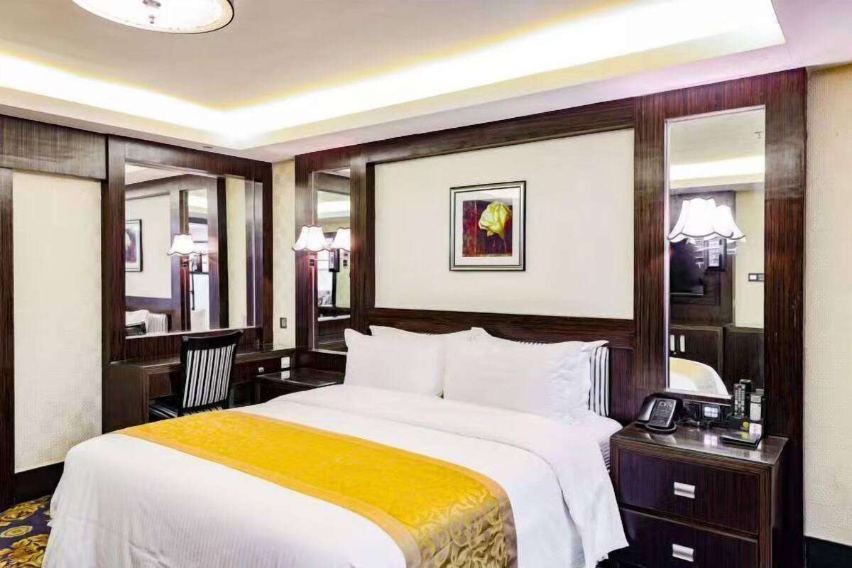 A hotel room with a large bed, a desk, a chair, a bedside table with a phone, and a mirror.