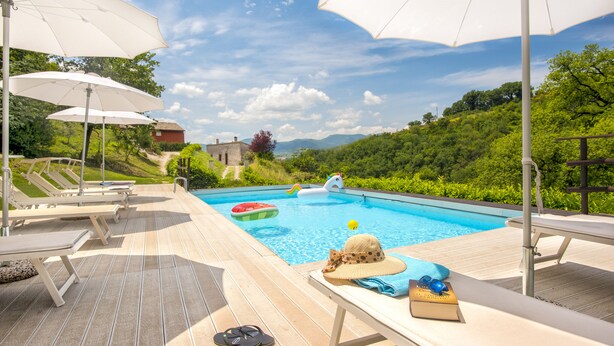 Un espace aménagé au bord de la piscine, avec des chaises longues, des parasols et une vue sur un paysage montagneux.
