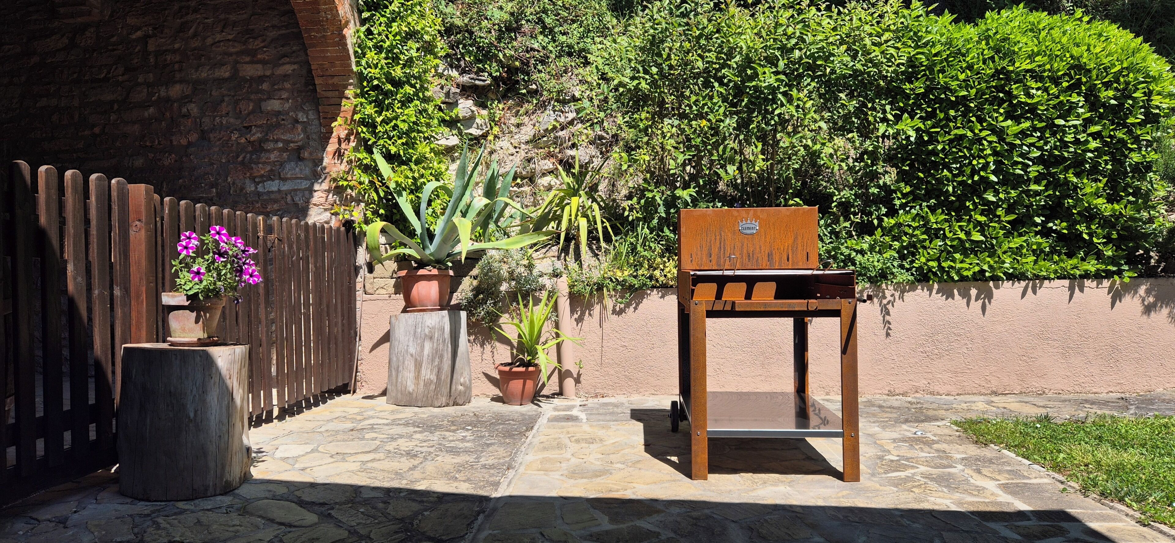 Une chaise en bois, une table en bois et des plantes en pot dans un espace jardin agrémenté d’un mur en briques et d’une clôture en bois.