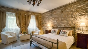 Une chambre avec un mur en pierre, un lit, une chaise, une table de chevet et une lampe.