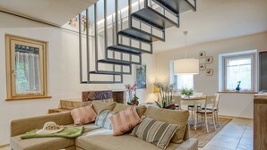 Un salon moderne avec un canapé d’angle, un coin repas comprenant une table et des chaises, et un escalier au design original.