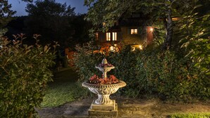 Un jardin agrémenté d’une fontaine, entouré d’une végétation luxuriante, avec une maison en arrière-plan.