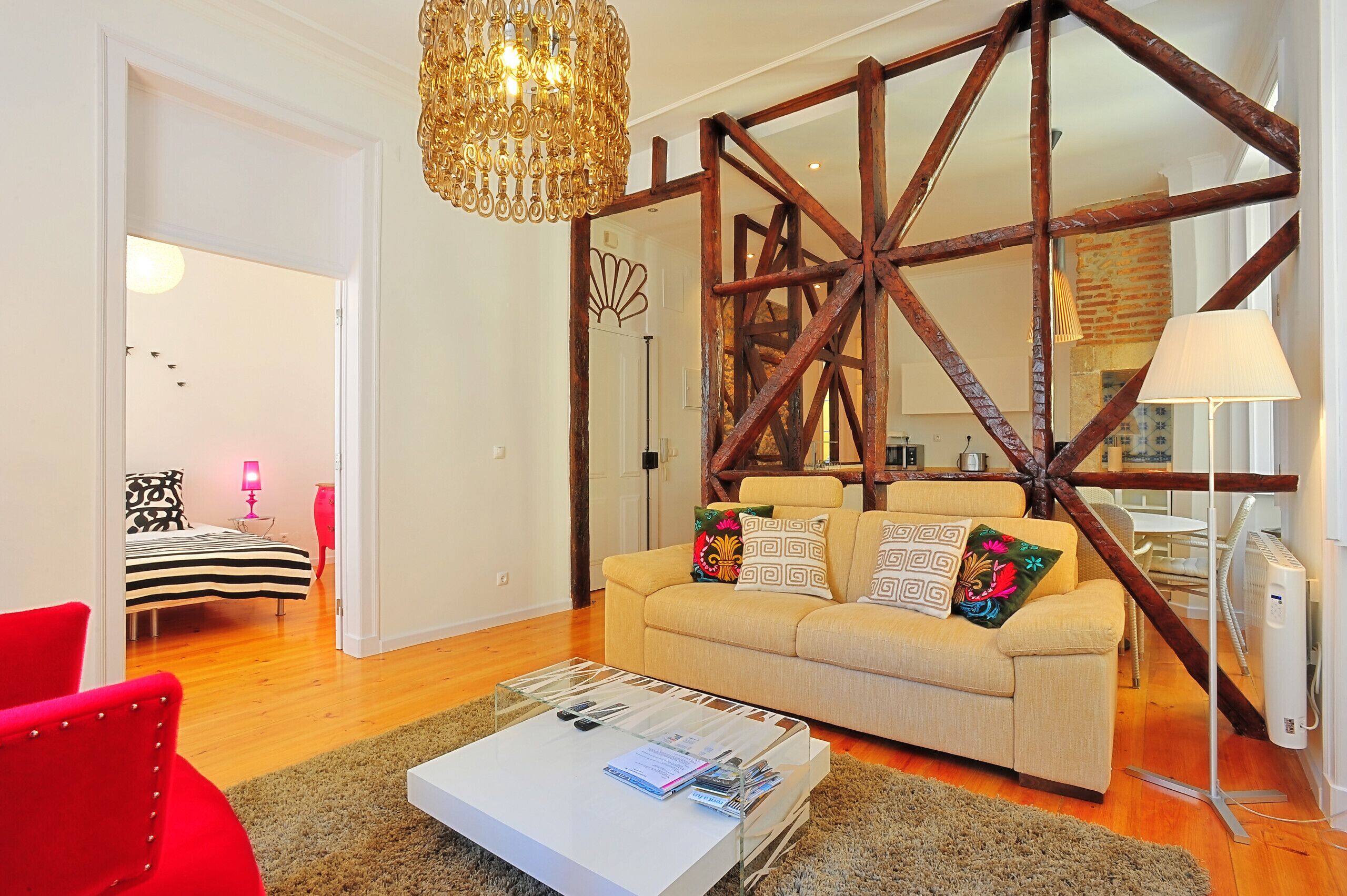 Un salon comprenant un canapé, une table basse, un fauteuil rouge et une structure en poutres apparentes.