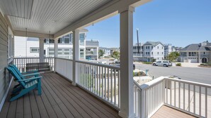 A wooden deck with two Adirondack chairs, a white railing, and a view of a residential street. - Beautiful, large home in Cape Shores! (Lewes)