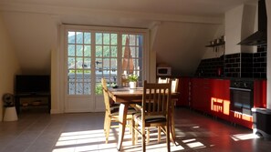 A dining area with a wooden table and chairs, a TV, and a kitchen with red cabinets and a stove.