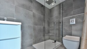Ein modernes Badezimmer mit einer gläsernen Duschkabine, einer Toilette und einem blauen Schrank.