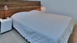 Ein Schlafzimmer mit schrägem Dach, einem Holzkopfende, einem Bett mit weißer Bettdecke, Nachttischlampen und einem Oberlicht.