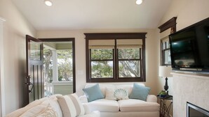 A living room with a beige sofa, a television mounted on the wall, and a window with blinds.