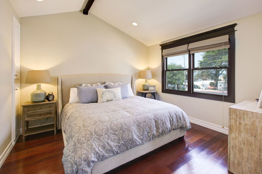 Un dormitorio con una cama grande, dos mesitas de noche con lámparas, una ventana con persianas y vistas al exterior.