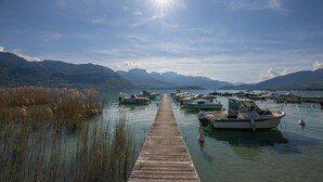 Un muelle de madera que lleva a un lago tranquilo con varias embarcaciones amarradas, rodeado de montañas.
