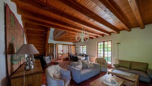 Un salón amplio con vigas de madera, una araña y un ventanal grande.