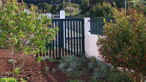 A garden with a gate leading to a white building, a mountain in the background, and a clear sky.