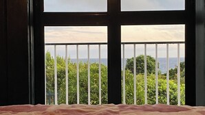A bedroom with a large window overlooking a balcony with greenery and a view of the ocean.