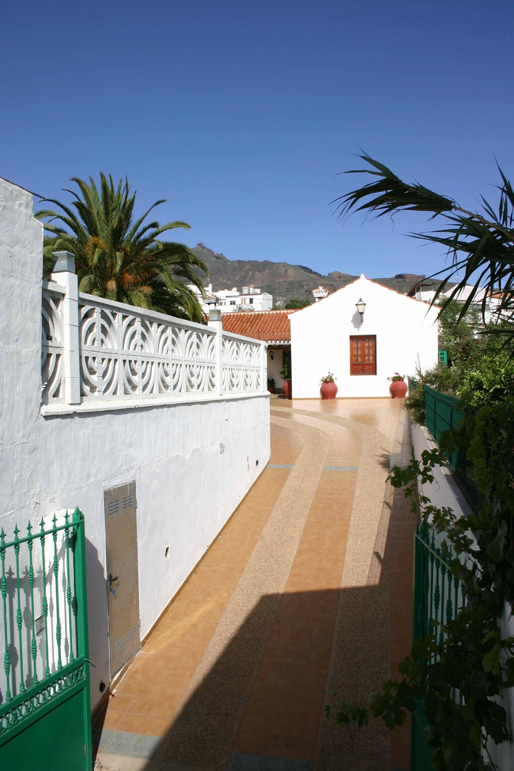 Un edificio blanco con una puerta roja, un muro blanco con una cerca decorativa y un camino empedrado que lleva a la entrada.
