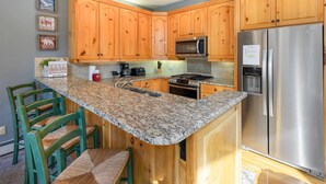 A kitchen with wooden cabinets, a granite countertop, a stainless steel refrigerator, and a built-in microwave.