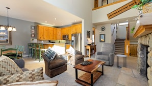 A spacious living area with a fireplace, a kitchen with wooden cabinets, and a dining area with chairs.