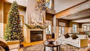 A spacious living room with a large Christmas tree, a fireplace, and a sofa.