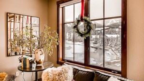 A cozy room with a large window, a mirror, a vase with plants, and a wreath on the window.