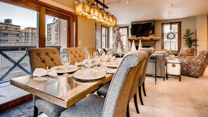 A dining area with a glass table, upholstered chairs, a chandelier, and a city view.