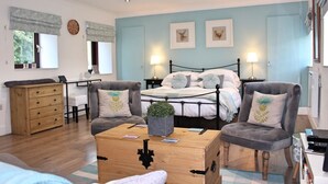A bedroom with a bed, two armchairs, a wooden chest of drawers, a desk, and a window with curtains. - A cute and cosy cottage, close to the train station. (dunblane)