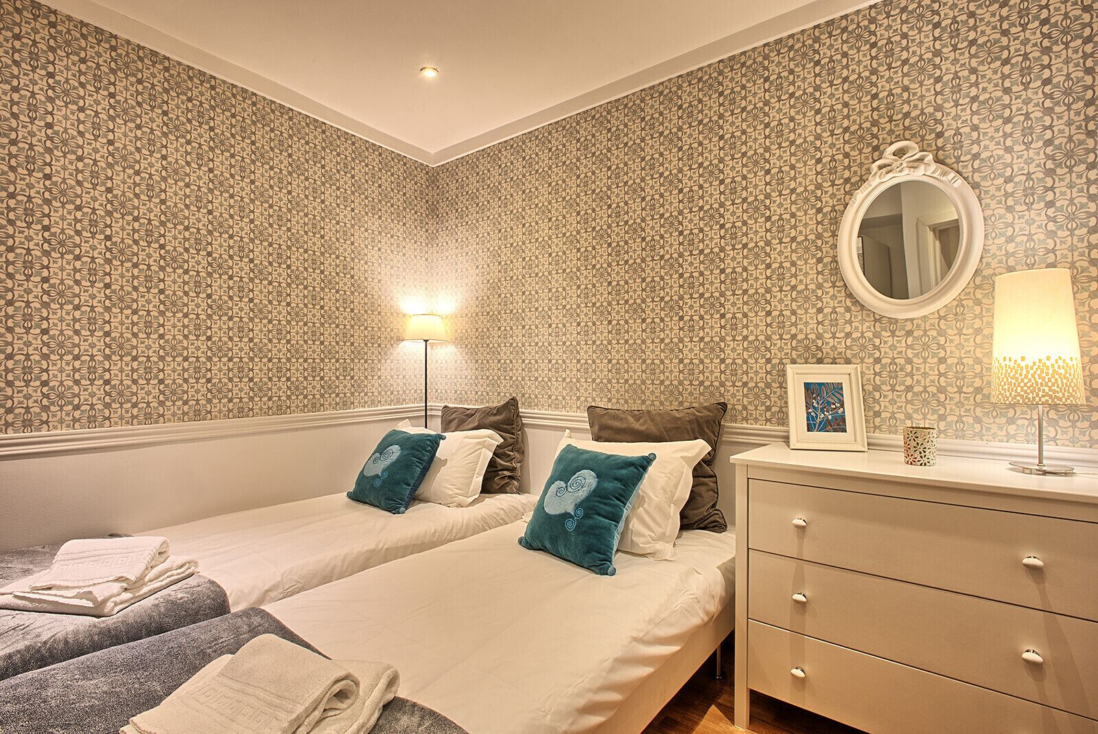 Une chambre d’hôtel avec deux lits, une table de chevet avec une lampe, un miroir et un tableau encadré.