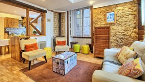 A spacious living room with a high ceiling, a stone wall, and a cozy seating area with a patterned ottoman and cushions. - Tv1 - Alfama Retreat | AC | 3 Bedrooms sleeps 10 walk everywhere (Lisbon)
